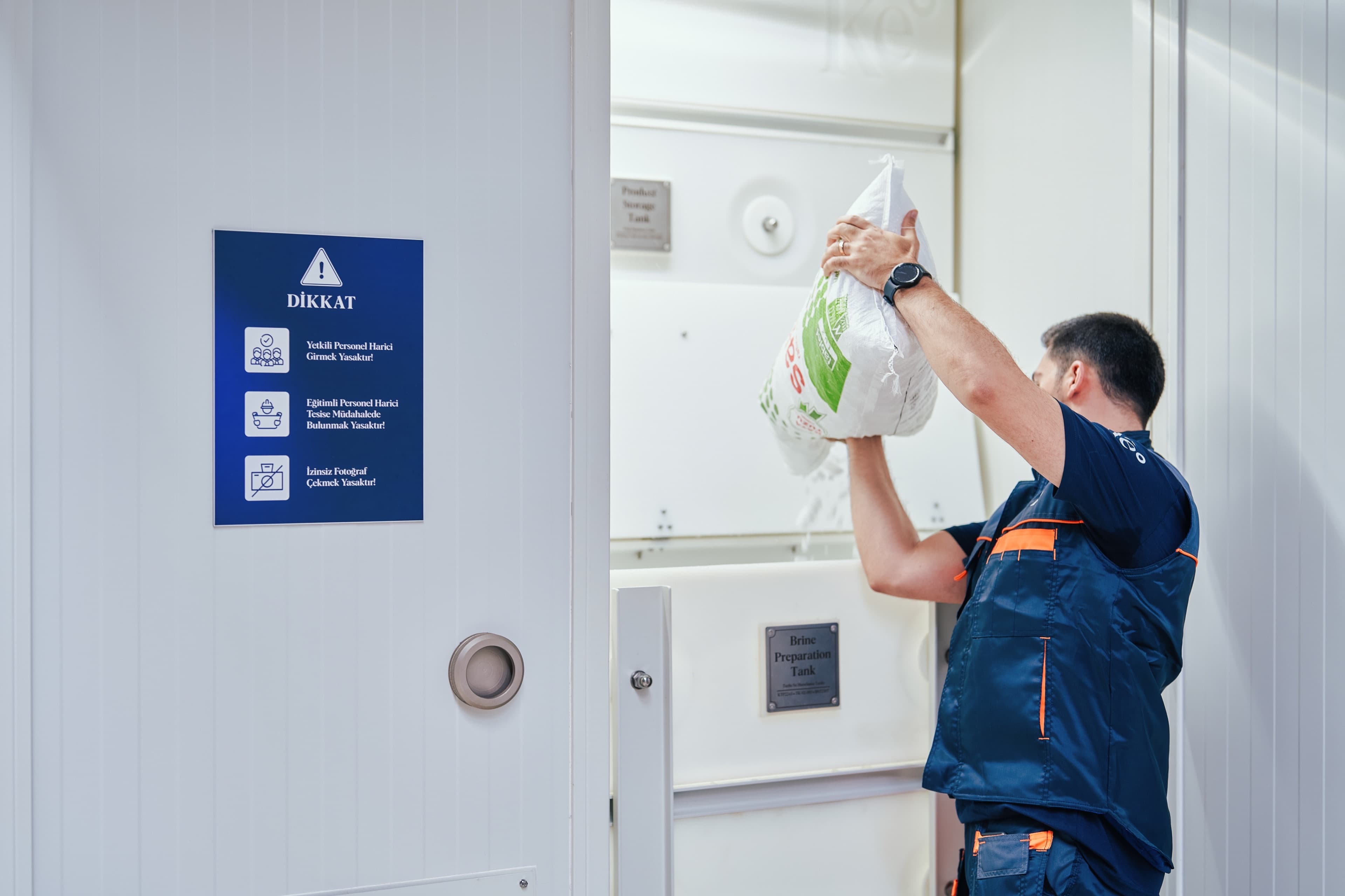 Operator emptying a salt bag into a HypoX CX brine saturator tank, with salt cascading into the water below