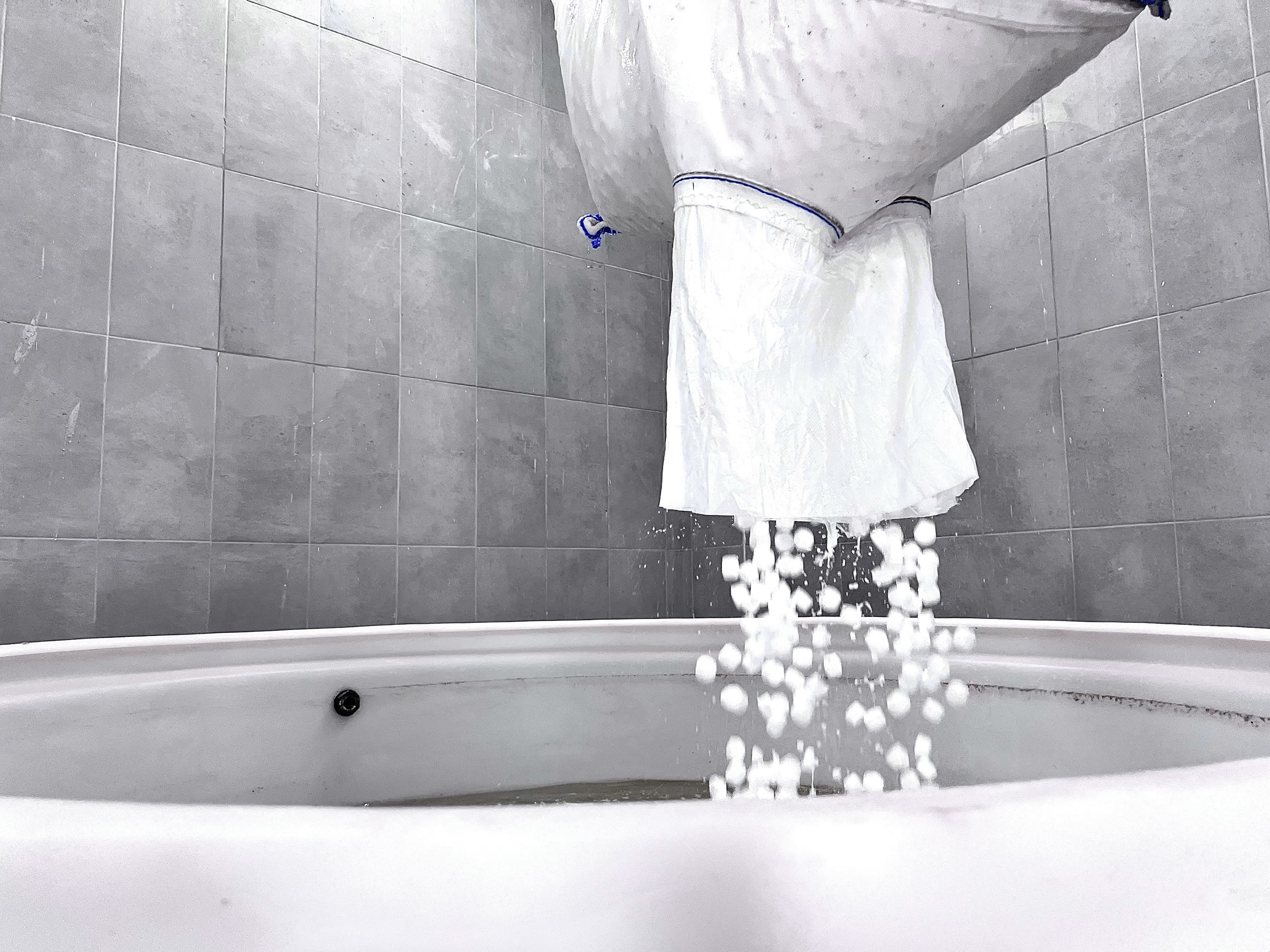 Operator emptying a salt bag into a HypoX LX brine saturator tank, with salt cascading into the water below