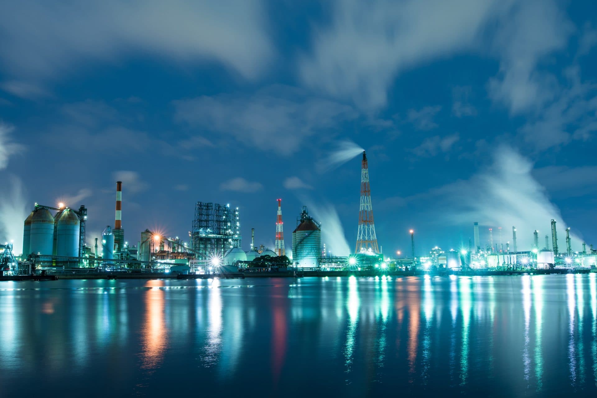 Coastal power plant illuminated at night, reflected on the water