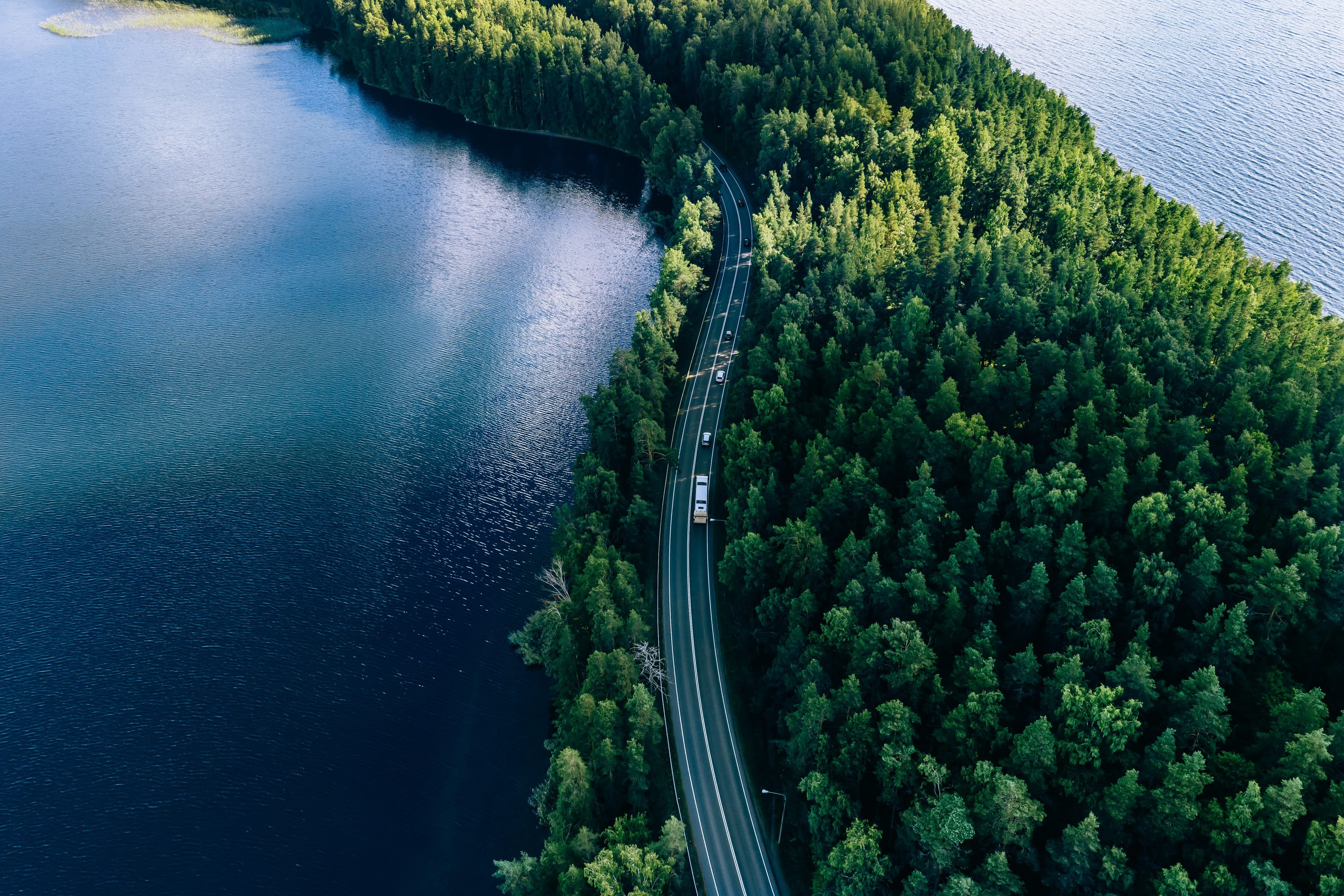 Aerial view of a road winding between a forest and a lake