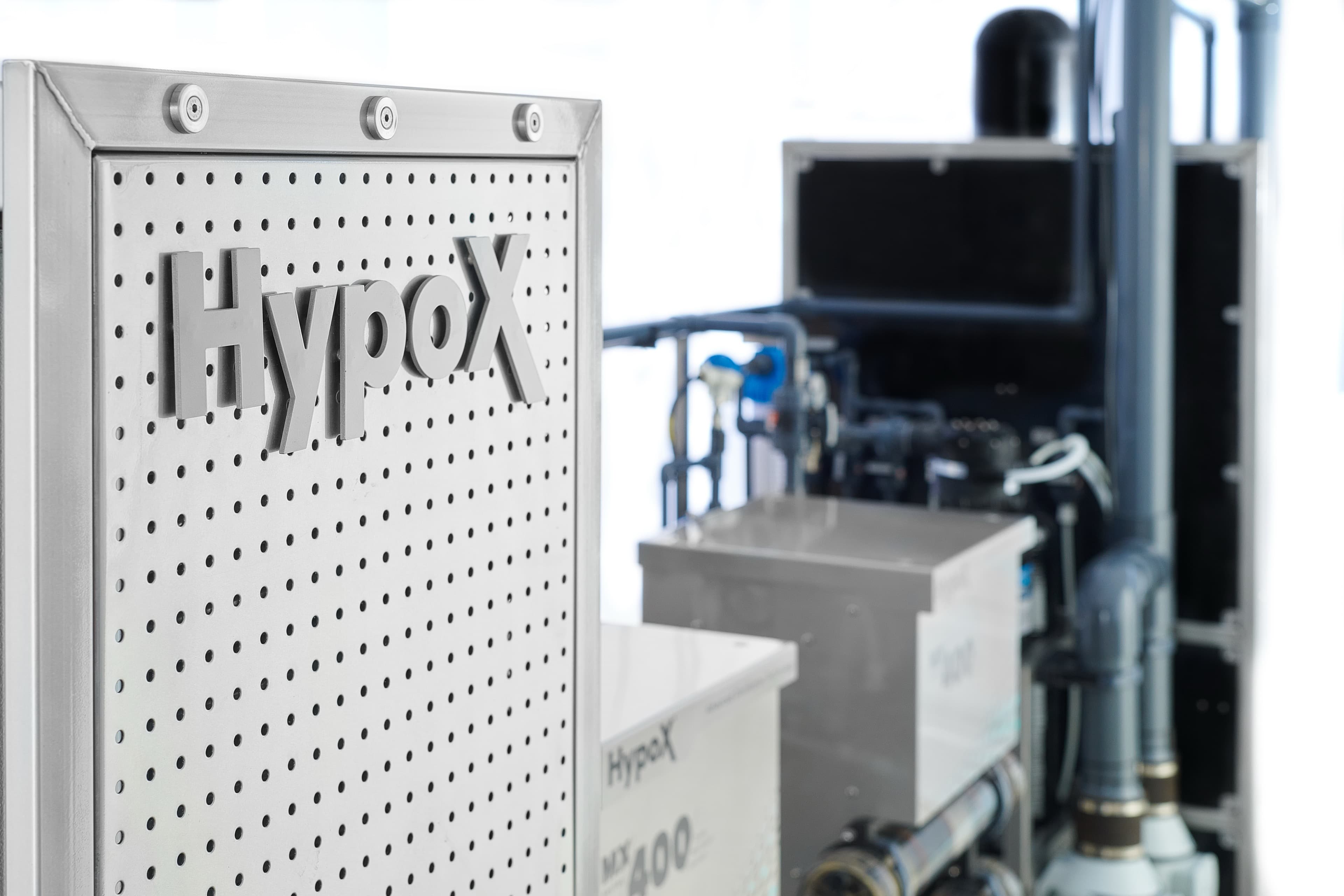 Close-up of a perforated stainless steel panel with raised HypoX lettering above dosing valves and instrumentation on a HypoX MX skid in a Kemisan production facility