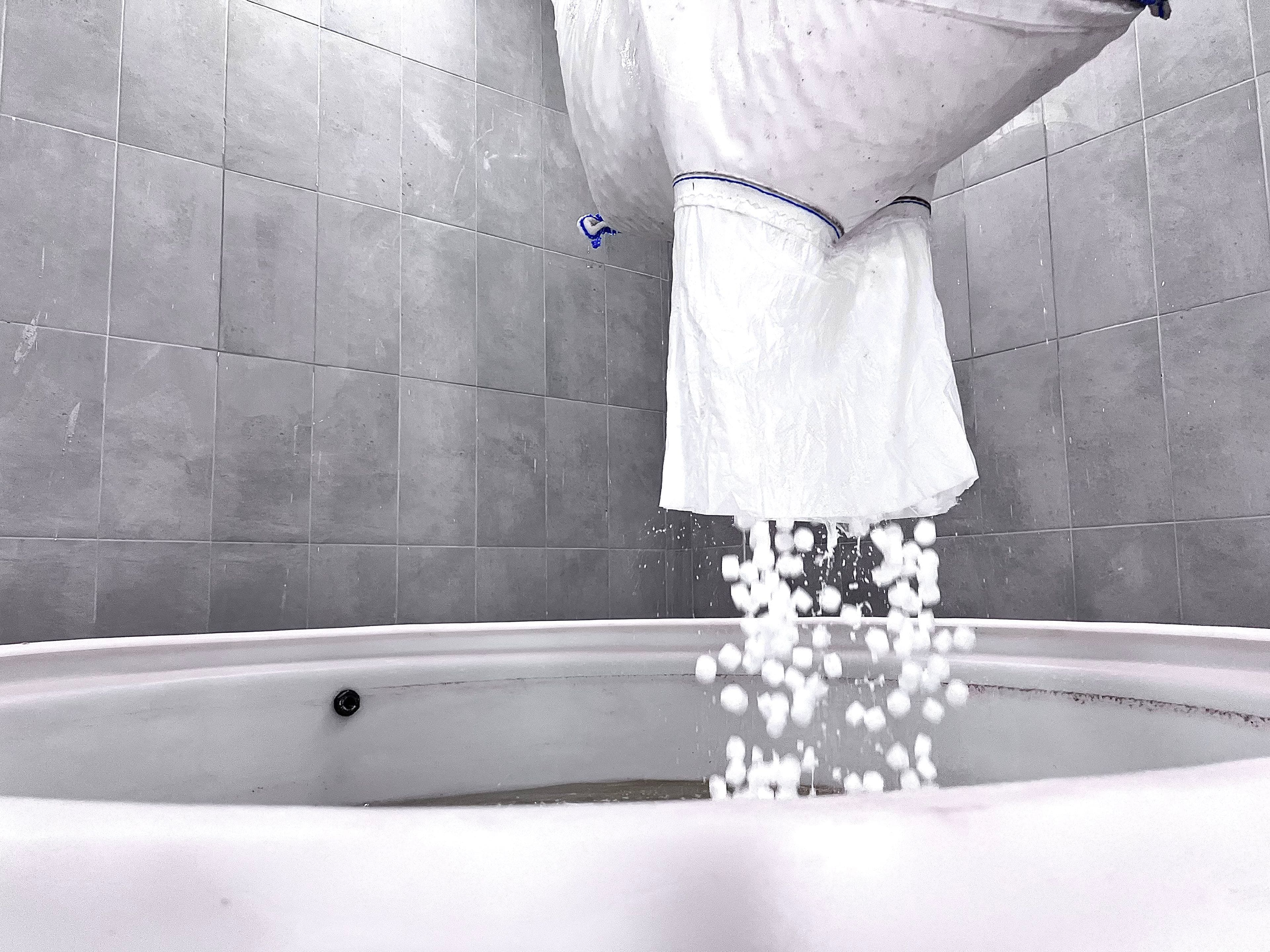 Operator emptying a salt bag into a HypoX PX brine saturator tank, with salt cascading into the water below